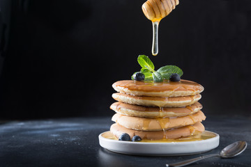 Sweet homemade stack of pancakes with pouring honey, fresh blueberry and mint in modern plate on...
