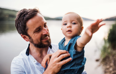 A father with a toddler girl outdoors by the river in summer.