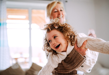 A portrait of small girl with grandmother having fun at home.