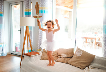 A small girl with a princess dress at home, holding a toy sword and jumping.