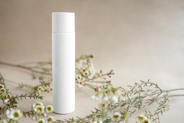 White cosmetic bottle on beige background decorated with white flowers
