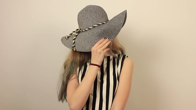 Portrait of cute funny girl covering face with round hat. Positive girl with fake moustache having fun. Grey wall on background.