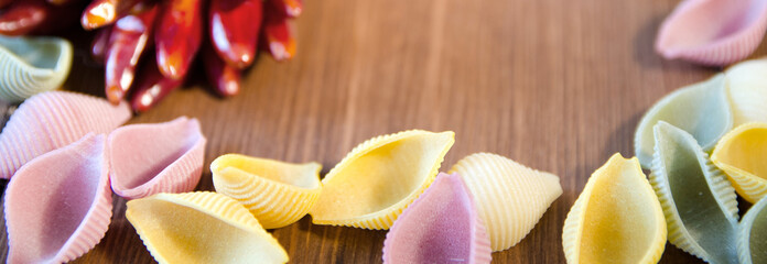Bunch of red dry Chili pepper with colored uncooked pasta on wooden background