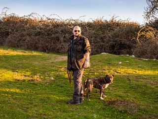 A strong adult man dressed in military uniform with a young dog of the American staffordshire breed in countryside in springtime