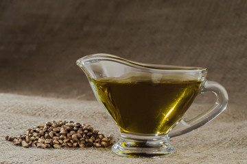 Hemp oil in a glass gravy boat and a handful of cannabis seeds on the background of burlap.