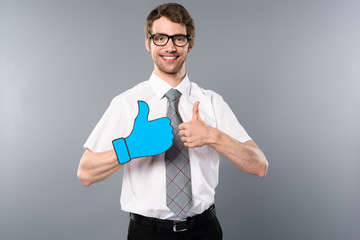 smiling businessman in glasses showing thumbs up on grey background