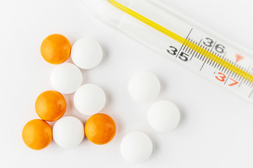 Thermometer, white and orange tablets close-up. Minimalistic image suitable as a background on the theme of medicine and health.