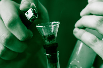Bong lighter for A man smokes cannabis weed, in his hands. Smoke on a black background. Concepts of...