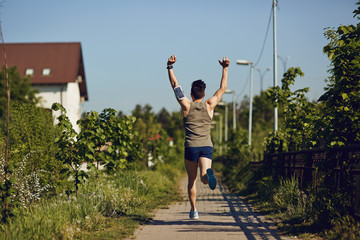 A male runner runs with his arms raised in the park.