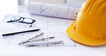 Concept of construction engineering. Building plan and yellow safety helmet on a table.