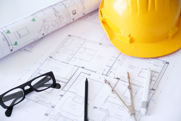Concept of construction engineering. Building plan and yellow safety helmet on a table.