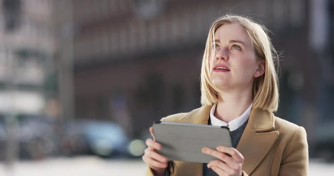 Attractive blonde using her tablet outside on the street