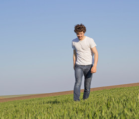 Naklejka na ściany i meble a teenager walking across a field covered with wheat shoots