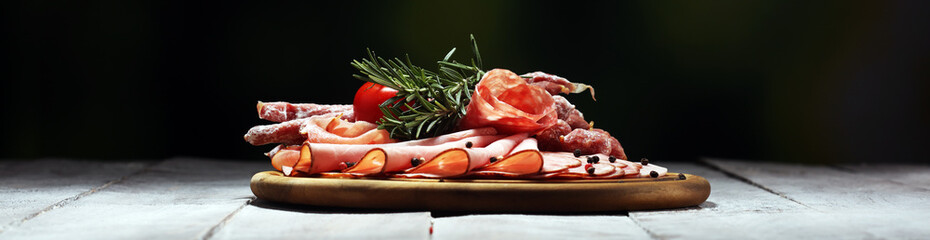 Food tray with delicious salami, pieces of sliced ham, sausage and salad. Meat platter selection.