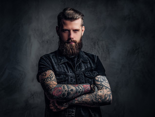 Portrait of a stylish bearded guy with tattooed hands. Studio photo against dark wall