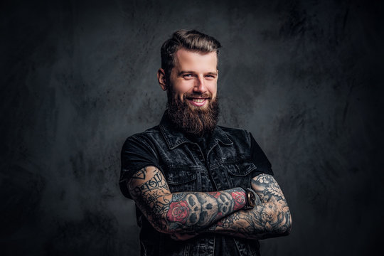 Portrait of a stylish bearded guy with tattooed hands. Studio photo against dark wall