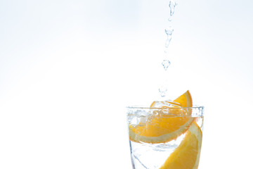 ice drink with orange and ice in the studio on a white background. a stream of water pours into the glass.