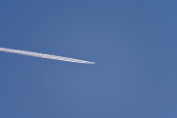 White airplane in blue clear sky with plane trails (jet trails)
