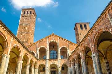 Fototapeta na wymiar Basilica of Sant'Ambrogio church brick building with bell towers, courtyard, arches, blue sky background, Milan, Lombardy, Italy