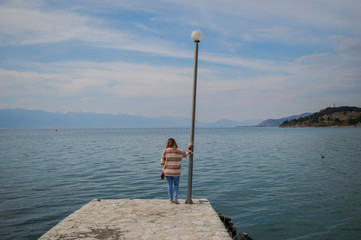 Fototapeta na wymiar Girl standing on the end of a pier watching the lake. Enjoying the silence near a lake.