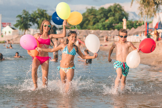 Happy children running together with balloons through the water