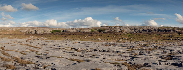Panorama image of Terrain in Burren national park, county Clare, Ireland, stone surface and cloudy blue sky.