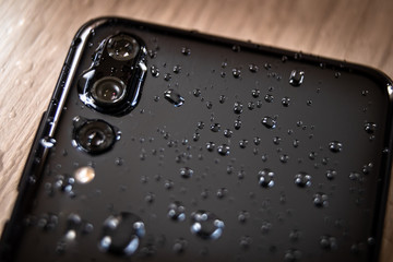 Back side of waterproof smartphone covered with drops of water