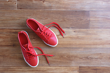 Red sneakers stand on a brown wooden floor. View from above.