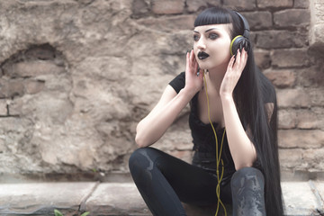 Urban goth girl listening to her favourite music over her big headphones, street in a city...