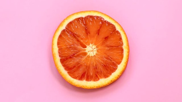 Blood orange slice rotating top view on pink background