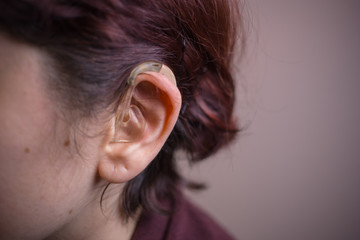 Close-up photo of a woman with hearing aid behind her ear. Sensory disability. Hearing disability