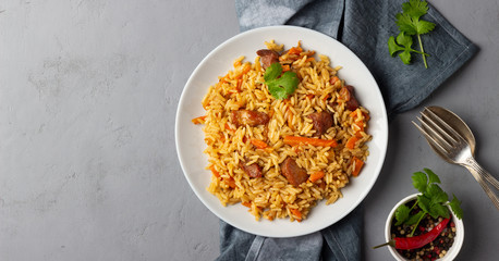 Traditional asian dish - pilaf from from rice, vegetables and meat in a plate on gray background. Top view with copy space.