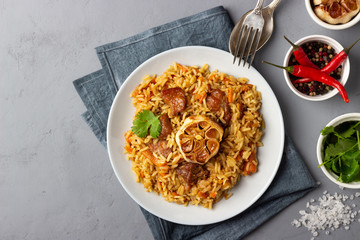 Traditional asian dish - pilaf from from rice, vegetables and meat in a plate on gray background. Top view.