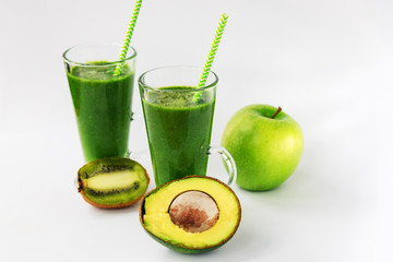 Two green smoothies in glass cups with straws, apple, kiwi, avocado on the white background, healthy food, raw vegan.