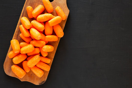 Peeled Baby Carrots On Rustic Wooden Board On Black Background, Top View. Overhead, From Above, Flat Lay. Copy Space.