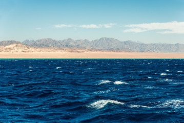 Seascape, view of the blue sea with high bald mountains in the background