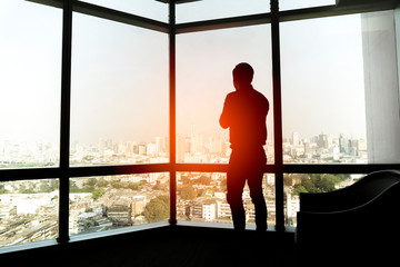Fototapeta na wymiar Silhouette of young Businessman looking at city through window