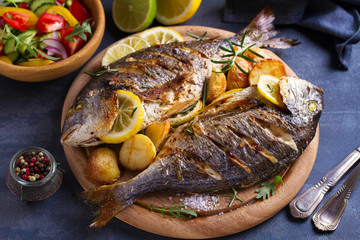 Grilled fish with roasted potatoes, lemon and rosemary on wooden tray