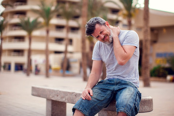 Man with neck pain sitting on bench outdoor. People, health care and medicine concept