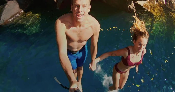 POV shot of young couple cliff jumping together into pristine blue water