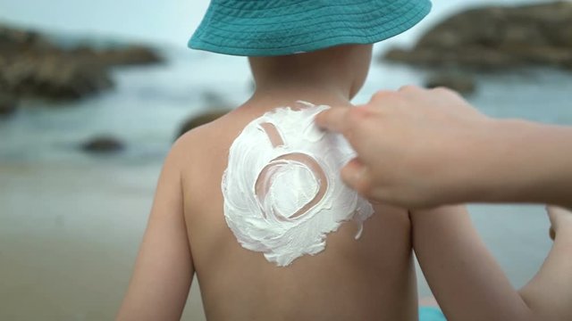 mom applying sunscreen lotion on body. Sun drawing in sunblock cream