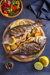 Grilled fish with roasted potatoes, lemon and rosemary on wooden tray. View from above, top