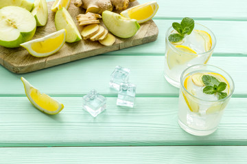 cold water with ice, ginger, mint, lemon and apple slices for summer healthy drink on mint green background