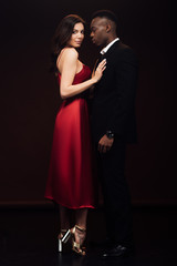 beautiful woman in fashionable red dress posing with african american man in suit isolated on black