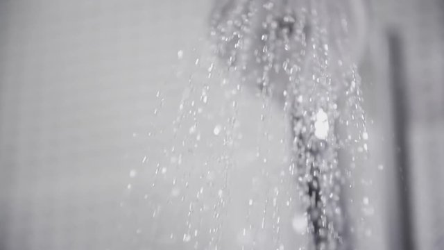 Close-up of water flowing from the shower head in bathroom, white tiles with black pattern on the walls, focus on falling water drops shot in slow motion