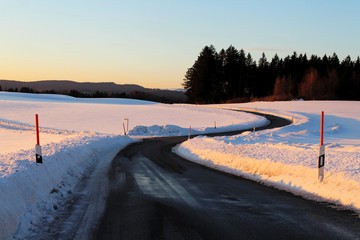 Kurvige Landstraße im verschneiten Allgäu bei Sonnenuntergang