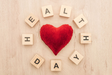 top view of cubes with health day lettering and toy heart on wooden background