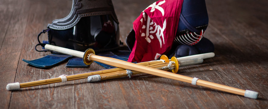 Kendo gloves, helmet and bamboo sword on a wooden surface.