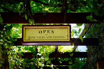 Wine sales and tasting signs at quaint winery entrance covered in grapevines.