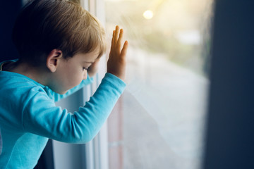 Little boy at home looking trough the window waiting for his mother to come back home